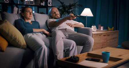 Bored sleepy couple watching TV at home and eating popcorn