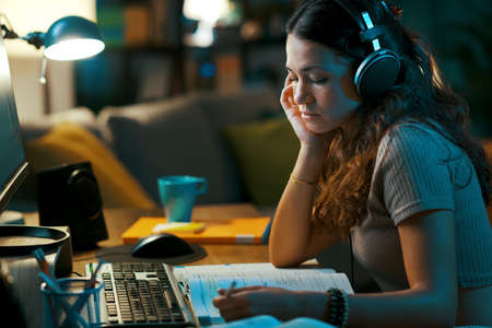 Young student taking online classes at home, she is wearing headphones and watching a video onlineの写真素材
