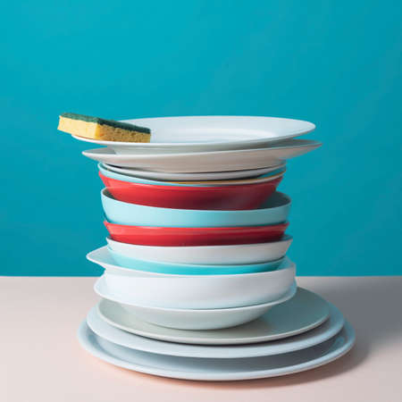 Stack of clean dishes and dish sponge on a tableの写真素材
