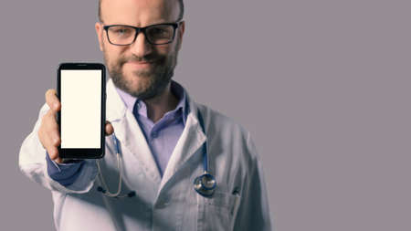 Smiling doctor showing a smartphone, healthcare apps and online doctor conceptの写真素材
