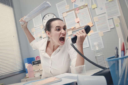Angry stressed businesswoman on the phone screaming out loud.の写真素材