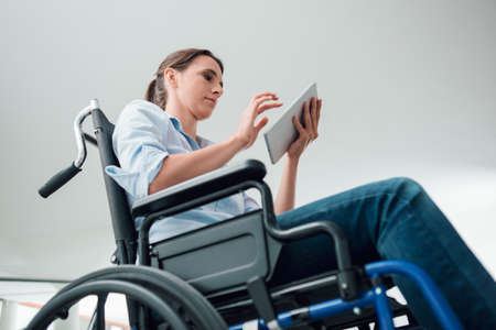 Confident young woman in wheelchair using a digital touch screen tabletの写真素材