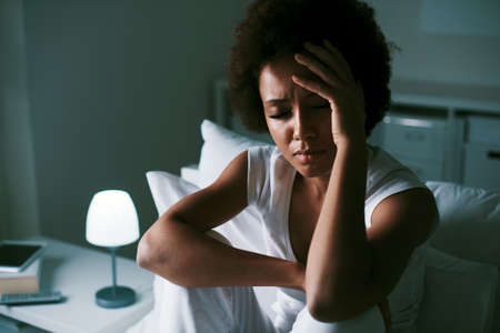 Sad depressed woman suffering from insomnia, she is sitting in bed and touching her forehead, sleep disorder and stress conceptの写真素材
