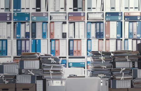 Stacks of files and paperwork in the office and bookshelves on the background: management and storage conceptの写真素材