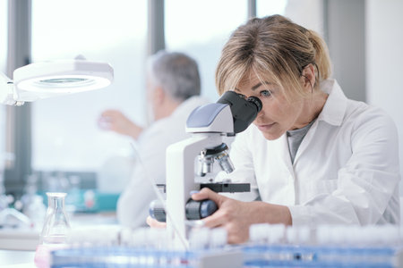 Female medical researcher working in the lab, she is sitting at desk and using a microscopeの写真素材