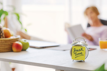Alarm clock with break time reminder and woman relaxing in the background