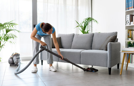 Young woman cleaning her home, she is vacuuming the floorの写真素材