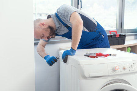 Professional repairman fixing a broken washing machine, home repair conceptの写真素材