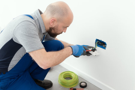 Professional electrician working on a home electrical system, he is installing a wall socket