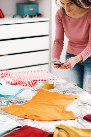 Woman taking pictures of her clothes on the bed, she wants to sell her second hand clothes onlineの写真素材