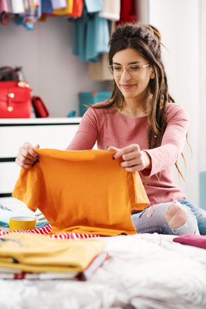 Young woman choosing clothes in her bedroom and organizing her wardrobeの写真素材