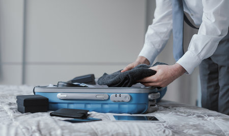 Corporate executive preparing for a business travel, he is packing his clothes and personal belongings in a trolley caseの写真素材
