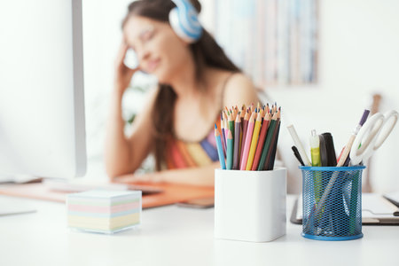 Creative young woman wearing headphones and working with computer, colored pencils in the foregroundの写真素材