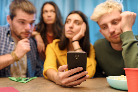 Group of friends thinking and feeling bored at home, one is holding a smartphone