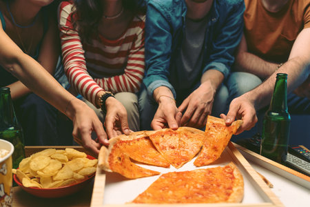 Group of friends sitting on the couch and eating pizza together at homeの写真素材