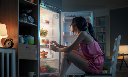 Woman suffering from the heat in summer, she is cooling herself in front of the open fridgeの写真素材