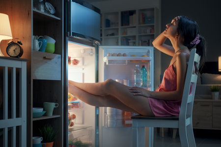 Woman suffering from the heat in summer, she is resting with her feet in the fridge and holding a water bottleの写真素材
