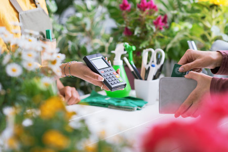 Customer at the florist shop, she is paying with her credit card, the shop owner is holding the POS terminal, hands close upの写真素材