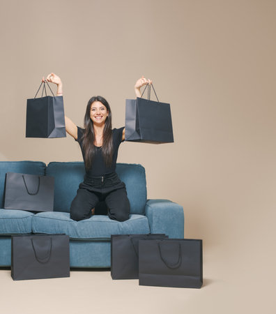 Happy woman sitting on a couch surrounded by black shopping bags: Black Friday saleの写真素材