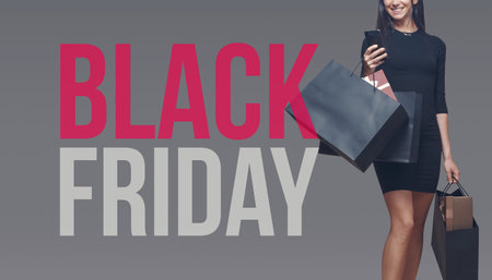Happy elegant woman holding shopping bags and a smartphone, Black Friday sale bannerの写真素材