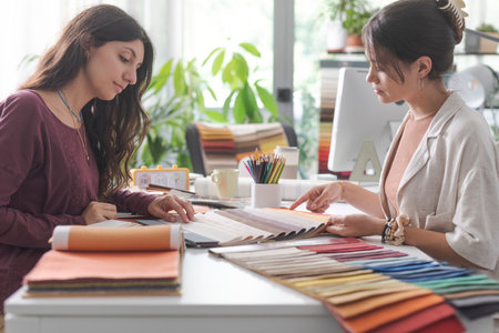 Interior designer and customer sitting at office desk, they are checking fabric swatches and picking colorsの写真素材