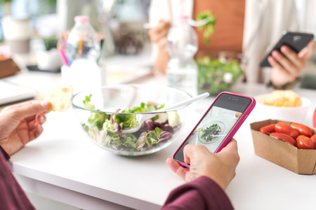 People having a lunch break, they are eating salad and using their smartphones, phone addiction conceptの写真素材