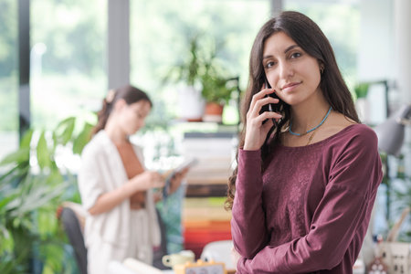 Professional young woman having a phone call with her smartphone and looking at cameraの写真素材