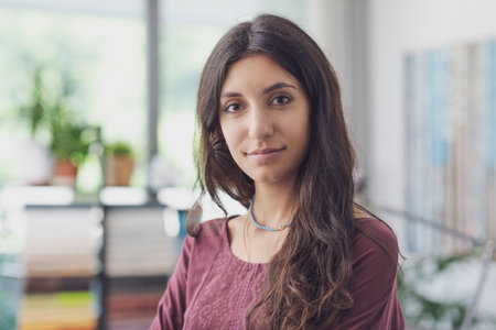 Happy young woman smiling and looking at camera, room interior with plants in the backgroundの写真素材
