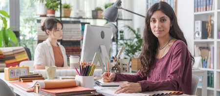 Professional interior designers working in the office, a woman is writing notes on her notebook and smiling at cameraの写真素材