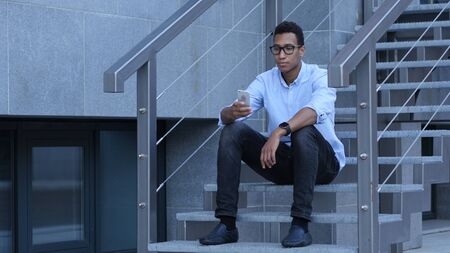 Using Smartphone for Online Browsing, Young Black Man Sitting on Stairsの写真素材