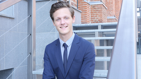 Smiling Young Businessman Sitting on Stairs Outside Officeの素材 [FY31084624063]