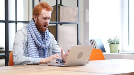 Beard Man Upset by Loss while Working on Laptopの写真素材