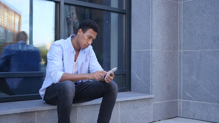 Outdoor Browsing on Smartphone, Sitting Young Black Handsome Manの写真素材