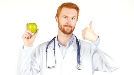 Portrait of a doctor showing an apple with the thumb up , white backgroundの写真素材