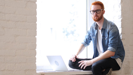 Man with Beard and Red Hairs Looking At Camera, Sitting in Windowの写真素材