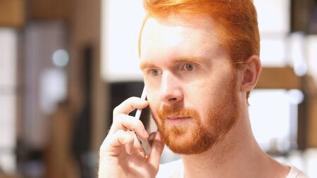Young Red Hair Beard Man Listening on smart phoneの写真素材
