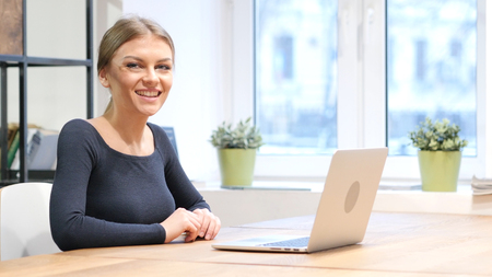 Girl Working on Laptop, Smiling toward Cameraの写真素材