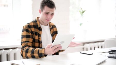 Upset Young Man Shocked by Loss on Tabletの写真素材