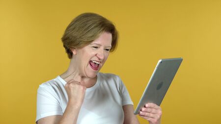 Old Woman Excited for Success while Using Tablet Isolated on Yellow Background