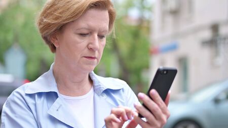 Old Woman Browsing Smartphone Standing Outdoorの写真素材