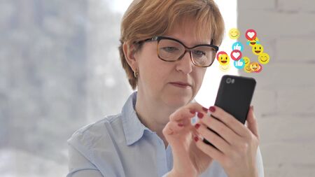 Senior Old Woman Watching a Live Stream on Smartphone, Emojis and Likesの写真素材