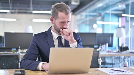 The Young Businessman having Coughing while working on Laptopの写真素材