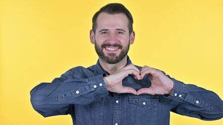 Portrait of Young Man making Heart Shape with Hand, Yellow Backgroundの写真素材