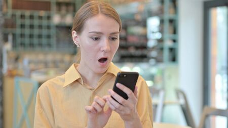 Portrait of Young Woman Reacting to Loss on Smartphoneの写真素材