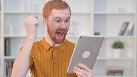 Portrait of Redhead Man Celebrating Success on Tabletの写真素材
