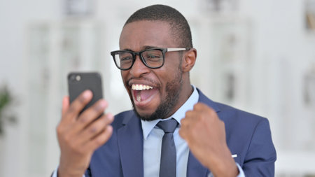 Portrait of African Businessman Celebrating Success on Smartphoneの写真素材