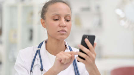 Portrait of Focused Young African Doctor using Smartphoneの写真素材