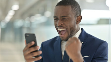 Portrait of African Businessman having Success on Smartphoneの写真素材