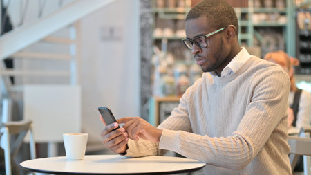 Attractive African Man using Smartphone in Cafeの写真素材