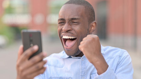 Portrait of Excited African Man Celebrating on Smartphoneの写真素材